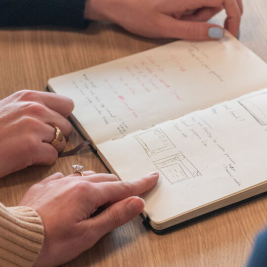 Photos de mains pointant un cahier sur une carnet posé une table en bois avec des graphiques représentant le fonctionnement d'Index Marketplaces