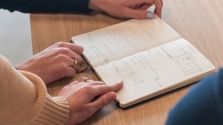 Photos de mains pointant un cahier sur une carnet posé une table en bois avec des graphiques représentant le fonctionnement d'Index Marketplaces